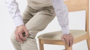 Äldre man med smärta i benen som reser sig från en stol